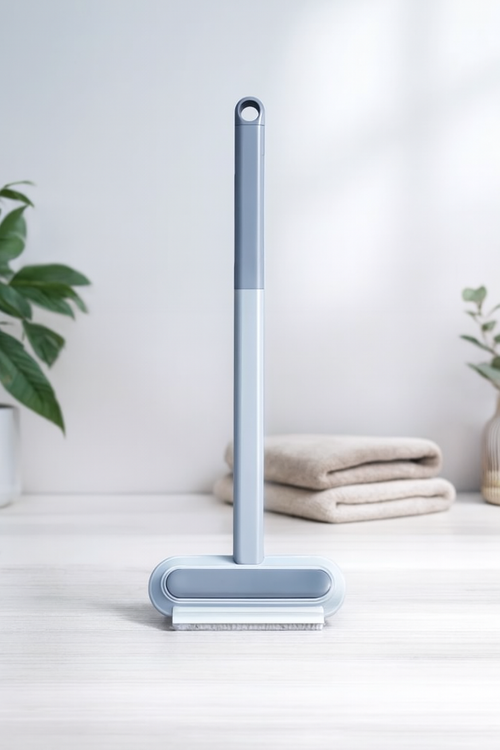 4-in-1 blue pet hair and dust removal brush standing upright on white surface with towels and plant in background